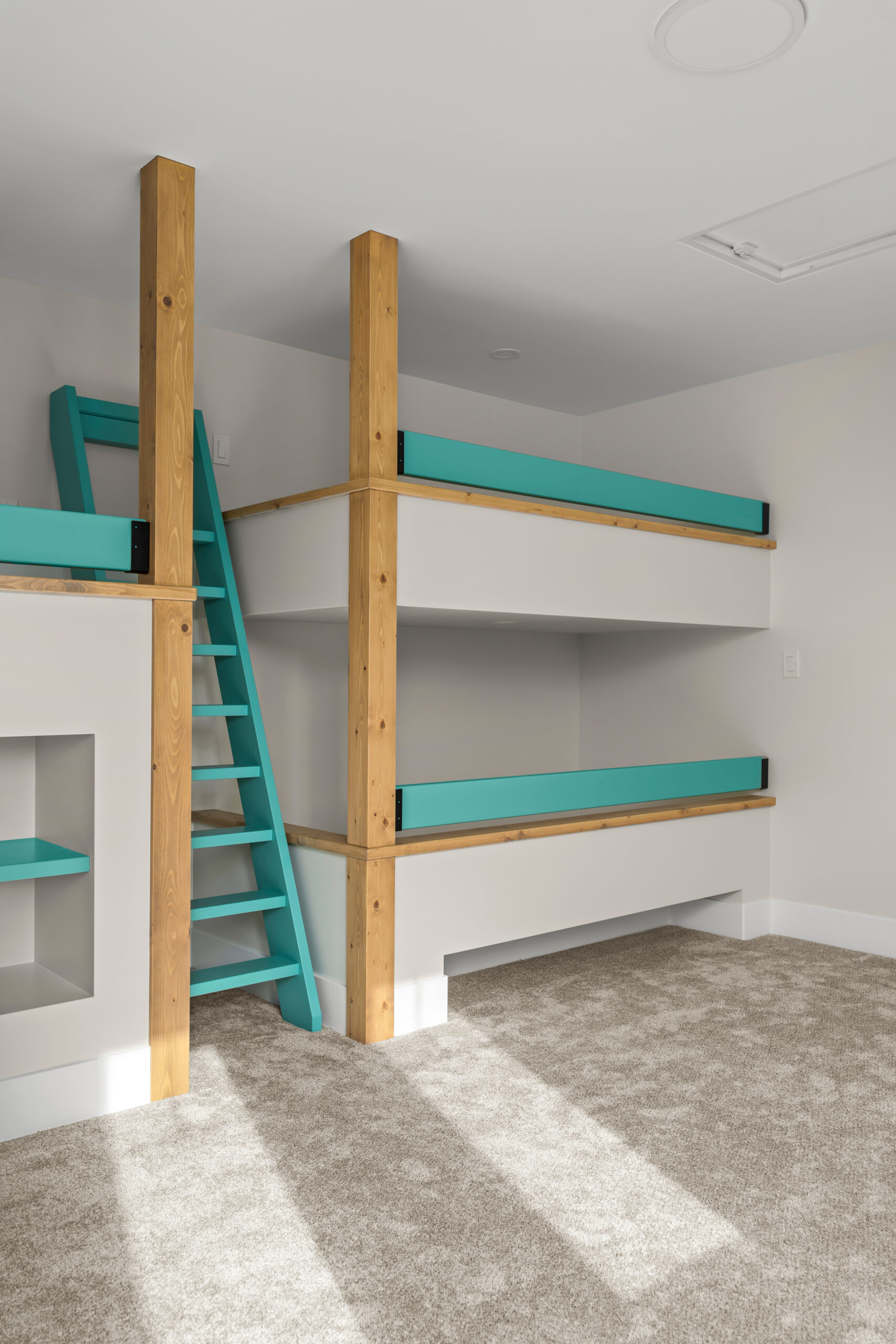 3 custom built bunk beds with a blue ladder between. There is a bookshelf under one bunk.