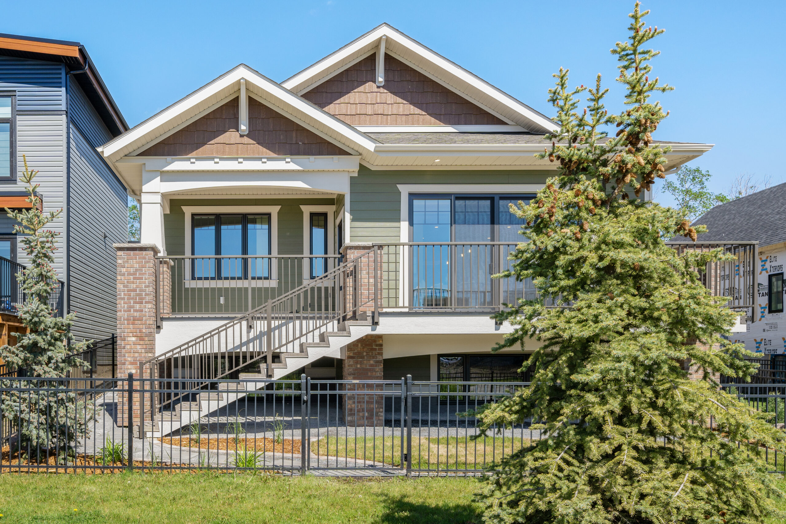 custom craftsman bungalow home built by Vleeming Custom Homes showing back deck and landscaping around the home. The home has black metal fencing around it