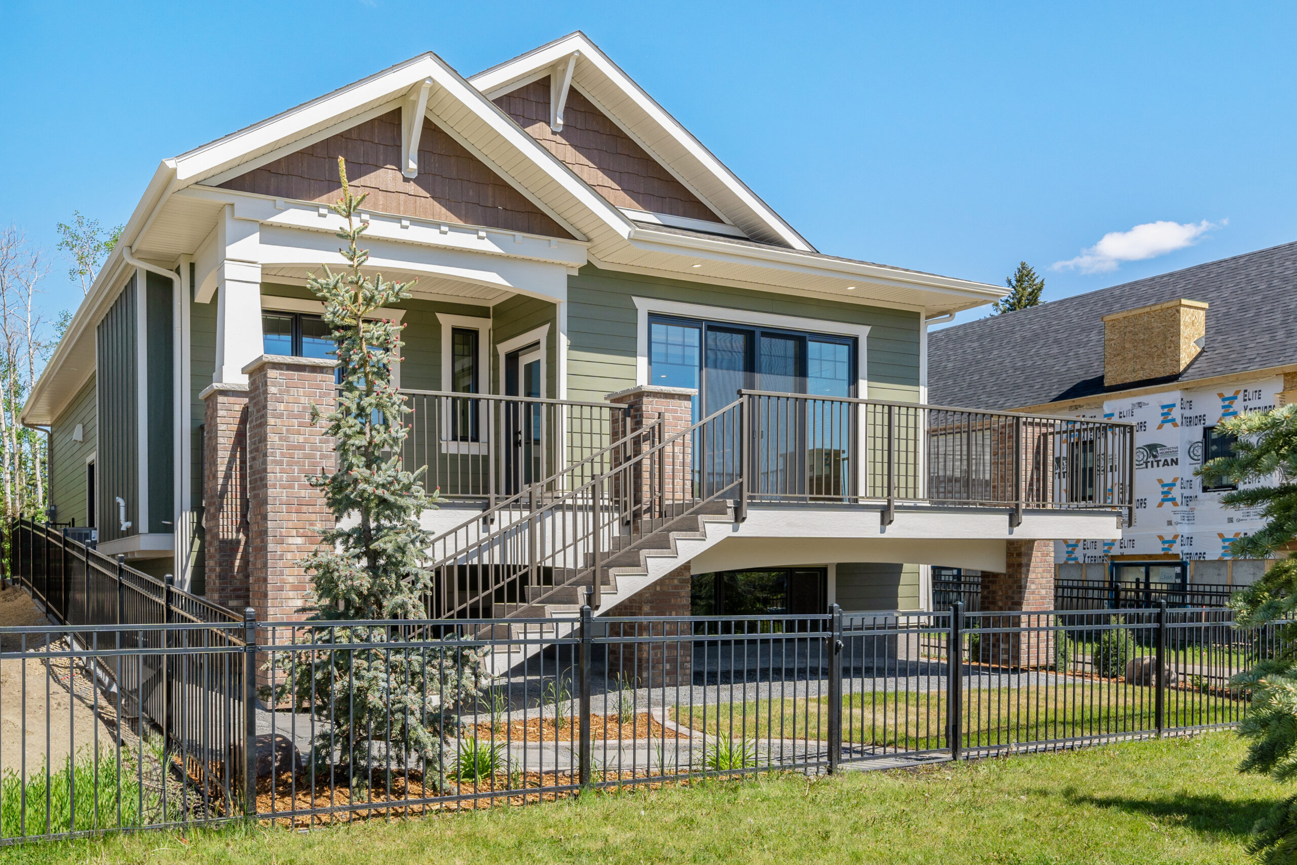 custom craftsman bungalow home built by Vleeming Custom Homes showing back deck and landscaping around the home. The home has black metal fencing around it